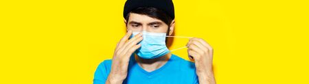 Portrait of young guy putting on a medical flu mask on face, protection against coronavirus or...