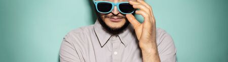 Close-up of young guy taking off sunglasses on background of aqua menthe color. Panoramic banner view.の写真素材