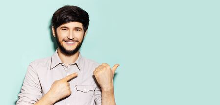Studio portrait of young guy showing with hands on empty background of aqua menthe color with copy...