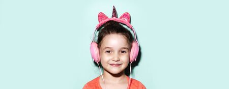 Portrait of smiling child girl listening the music with headphones on background of aqua menthe color. Panoramic banner view concept.の写真素材