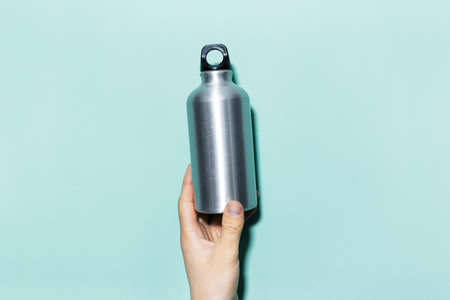 Close-up of male hand, holding aluminum, thermo water bottle on the background of cyan color.の写真素材