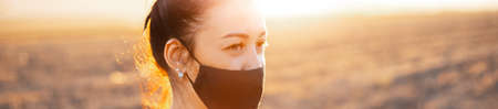 Outdoors portrait of aged woman, wearing respiratory face mask. Background of sunset.の写真素材