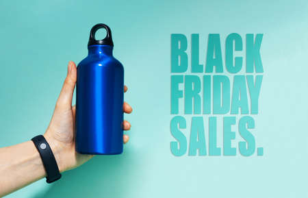 Black Friday sales text near female hand holding aluminum thermo water bottle of blue. Background of cyan, Aqua menthe color.の写真素材