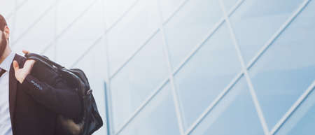 Businessman holding a briefcase. Panoramic background of blue skyscraper window with copy space. Business concept.の写真素材