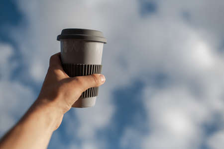 Close-up of male hand holding coffee mug on background of sunny sky.の写真素材