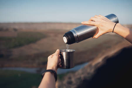 Close-up of female hands, pouring tea into the steel cup from , on outdoor background. Travel concept.の写真素材