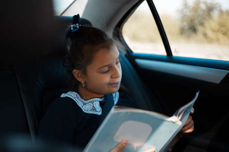 Child girl looking into the book in the car, wearing school form. On on the way home after school.の写真素材