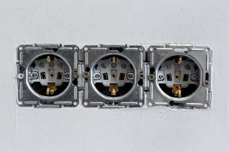 Close-up of three sockets on background of grey wall.