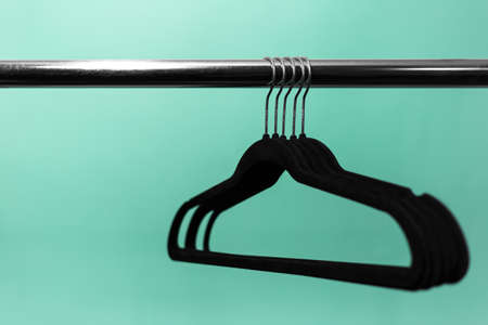 Close-up of clothes rack with black empty hangers on background of aqua menthe color. Minimalistic concept.の写真素材