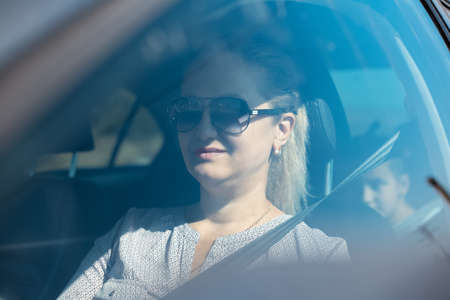 Portrait through car window, of woman driving. Wearing sunglasses.