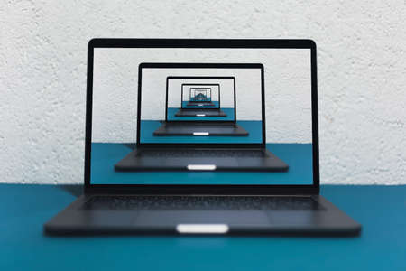 Enigmatic surrealistic optical illusion. Close-up of modern laptop on blue table, background of grey textured wall.の写真素材