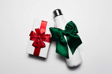 Close-up of gift box and reusable steel thermo water bottle with red and green bows. Isolated on white background.の写真素材