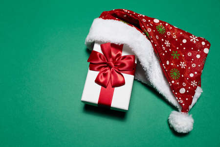 Top view of white gift box with red bow wearing Santa hat on background of green color with copy space.の写真素材