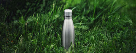 Panoramic photo of reusable steel thermo water bottle in green grass.