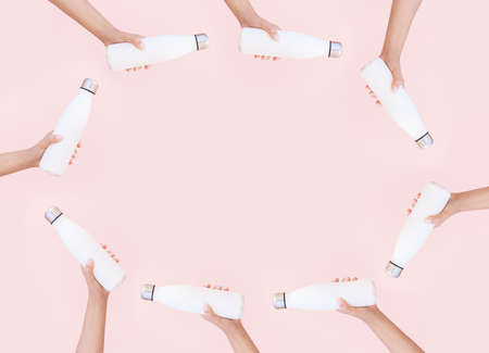 Female hands holding white eco reusable steel thermo water bottles on background of pastel pink color with copy space in the middle.の写真素材