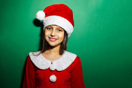 Studio portrait of smile children girl wearing red costume of Santa Claus on green background.の写真素材
