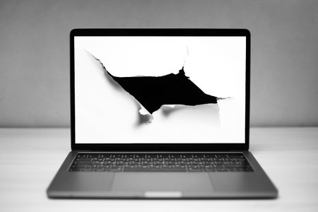 Close-up of laptop with hole in paper on screen, textured background of grey.