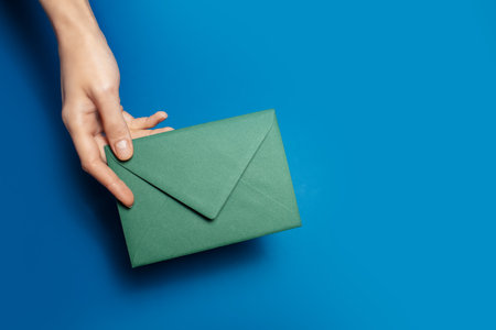 Close-up of female hand holding a green paper envelope on background of blue color.の写真素材