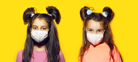 Studio portrait of two teenage girls wearing medical mask on yellow background. Prevention of coronavirus and covid-19. Panoramic photo.の写真素材