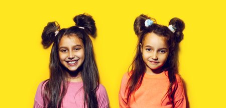 Studio portrait of two cheerful teenage girls on background of yellow color.の写真素材