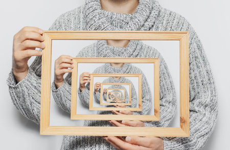 Enigmatic surrealistic optical illusion, young man holding frame on white background.