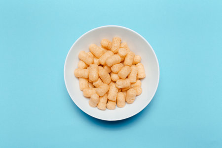 Top view of white bowl with corn puffs on blue background.の写真素材