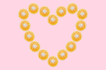 Orange fruits in shape of heart on pastel pink background.の写真素材