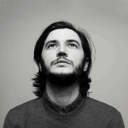 Black and white portrait of young guy with long hair looking up on  grey background.