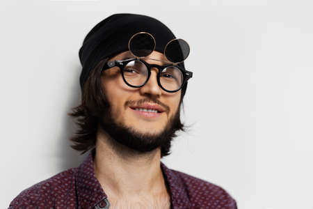 Studio portrait of smiling guy on white background. Wearing round glasses and hat.