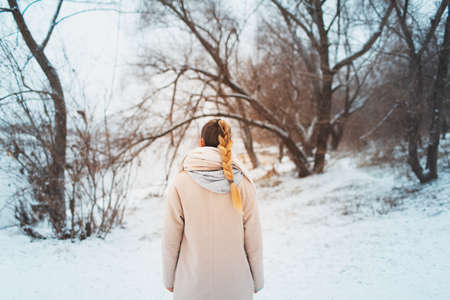 Back view of young woman with braid hairstyle wearing coat on background of snowy trees of forest.の写真素材