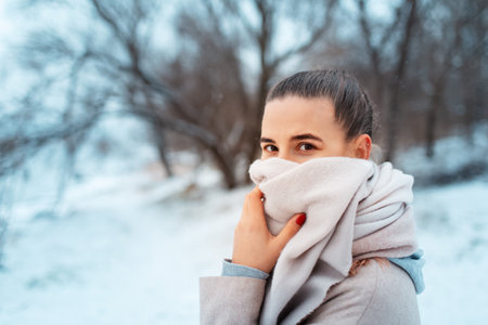 Portrait of young girl in park in winter day, wearing scarf, on background of blurred trees.の写真素材