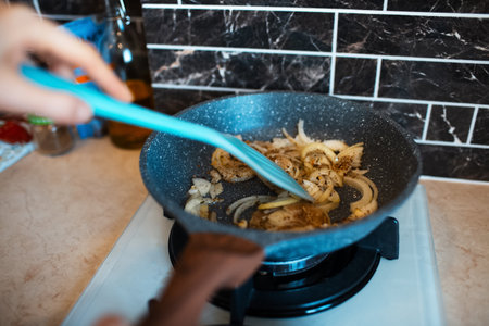 Close-up picture of female hand, stirring fried chopped onions on the pan, in the kitchen area.の写真素材