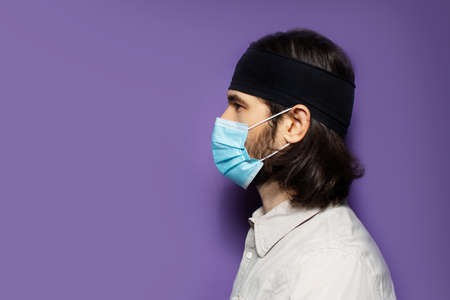Studio portrait of young brunette guy,  from one side, with long hair and protective medical mask,...