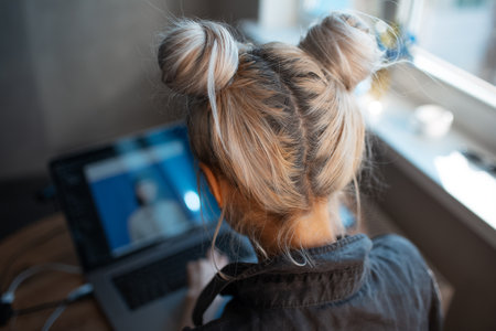Close-up of back view portrait of young girl, with two funny hair buns, working on the laptop.の写真素材