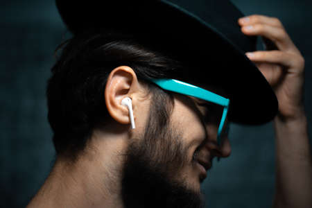 Close-up portrait of young man, listen the music with wireless earphones, wearing blue sunglasses...