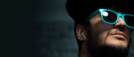 Close-up portrait of young man with wireless earphones, looking up wearing blue sunglasses on black background.の写真素材