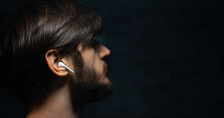 Close-up portrait of young man using wireless earphones on black background with copy space.の写真素材
