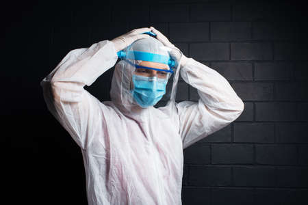 Studio portrait of tired doctor wearing PPE  , on the background of black brick wall. Pandemic concept.の写真素材