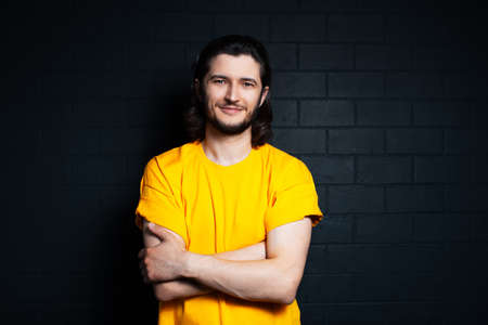 Portrait of young smiling man in yellow shirt on background of black brick wall.の写真素材