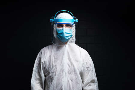 Studio dark portrait of young doctor man wearing PPE suit against coronavirus and covid-19. Background of black brick wall.の写真素材
