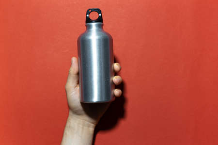 Close-up of male hand holding reusable aluminum thermo water bottle on background of red textured wall.の写真素材