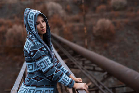 Portrait of young hooded girl standing on abandoned rusty bridge with perspective background. Artistic fashion concept.の写真素材