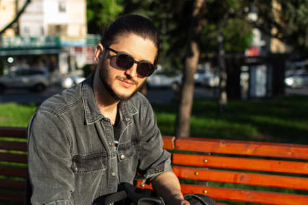Portrait of young guy sitting on bench in the park.