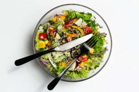 Top view of vegan salad in glass bowl with black fork and knife on white background.の写真素材