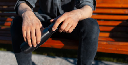 Close-up of male hands, holding steel reusable thermo water bottle.の写真素材