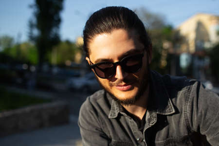 Outdoor portrait of young smiling man wearing sunglasses on background of blurred street.の写真素材