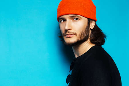 Studio portrait of young serious guy wearing orange hat on blue background.の写真素材