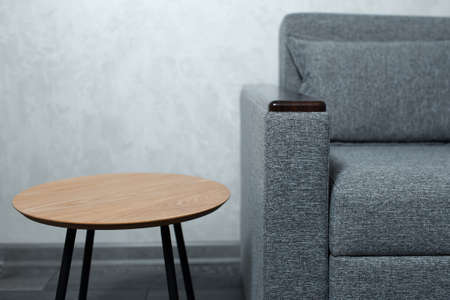 Close-up of small wooden round table near grey sofa on background of textured wall.の写真素材