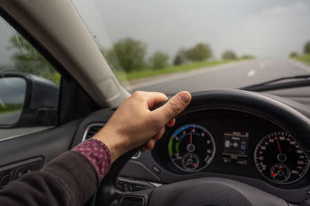 Close-up of male hand holding steering wheel, driving the car. Background of blurred road.