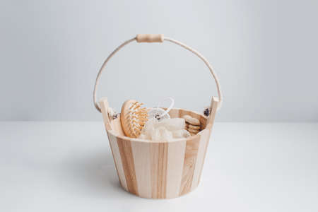 Close-up of small wooden bucket with set of bath accessories; hairbrush, washcloth, pumice stone and massager tool. White studio background.の写真素材